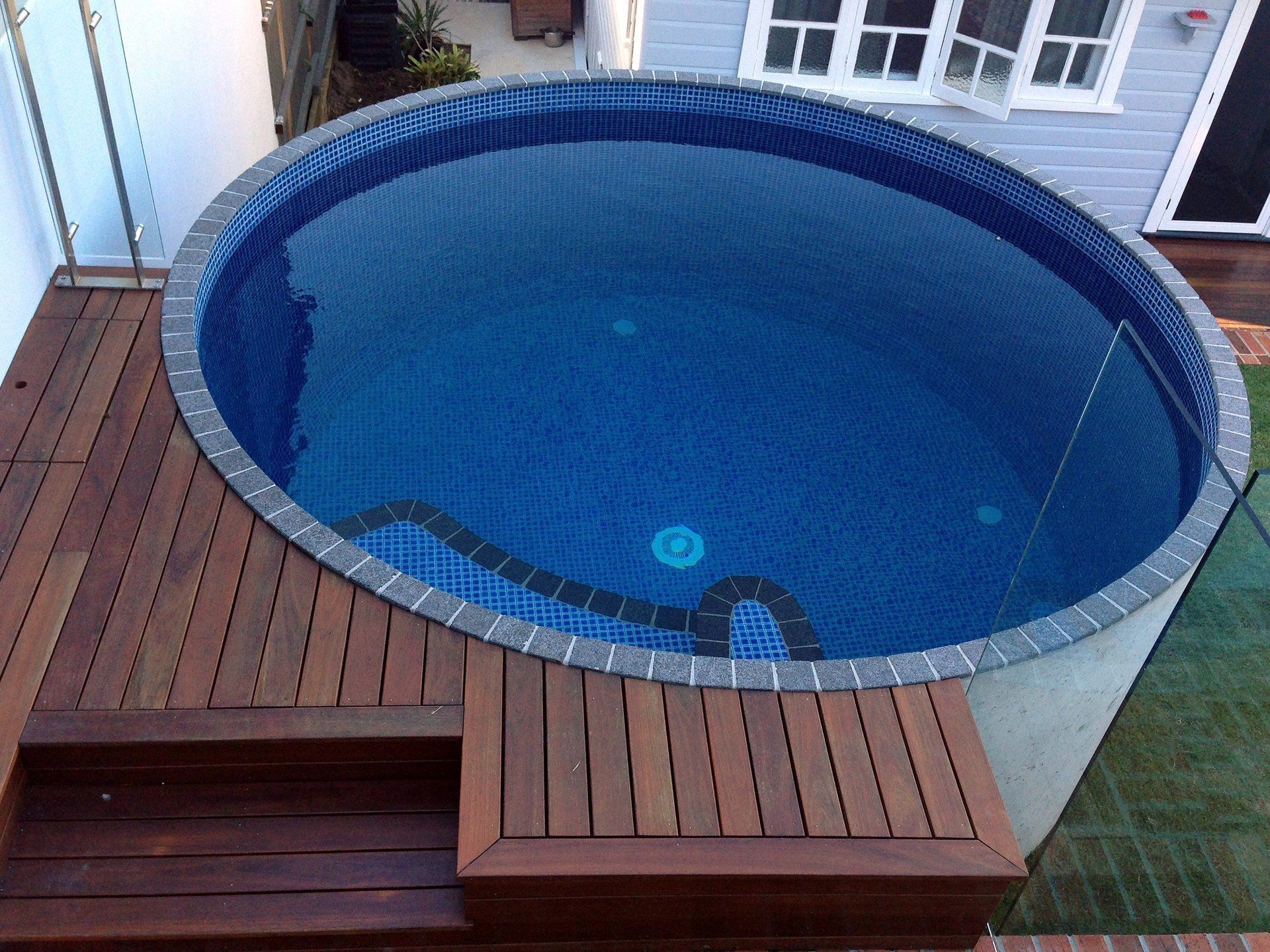 A large round swimming pool is sitting on a wooden deck
