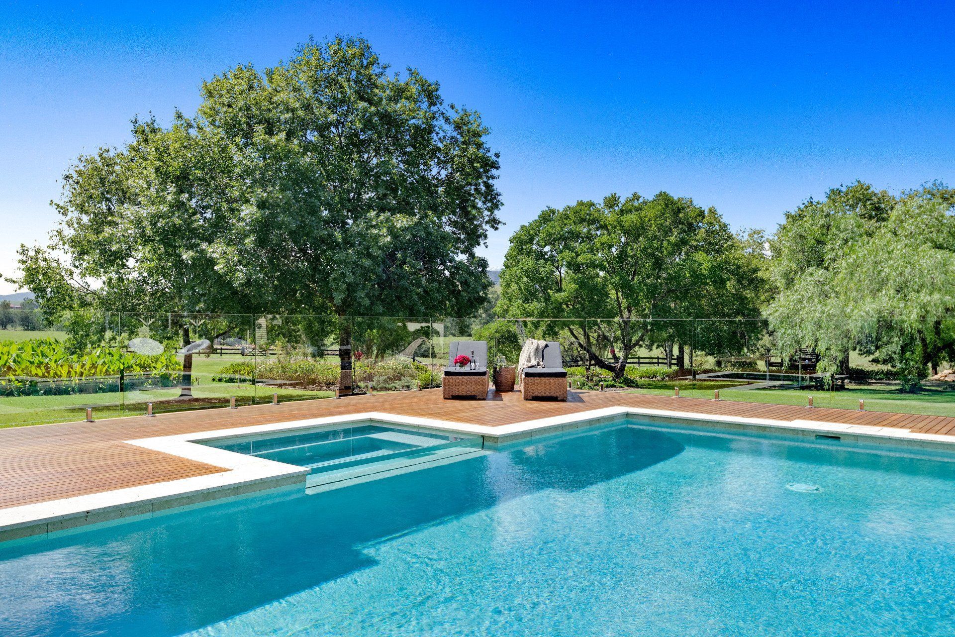 A large swimming pool surrounded by trees and chairs on a sunny day.