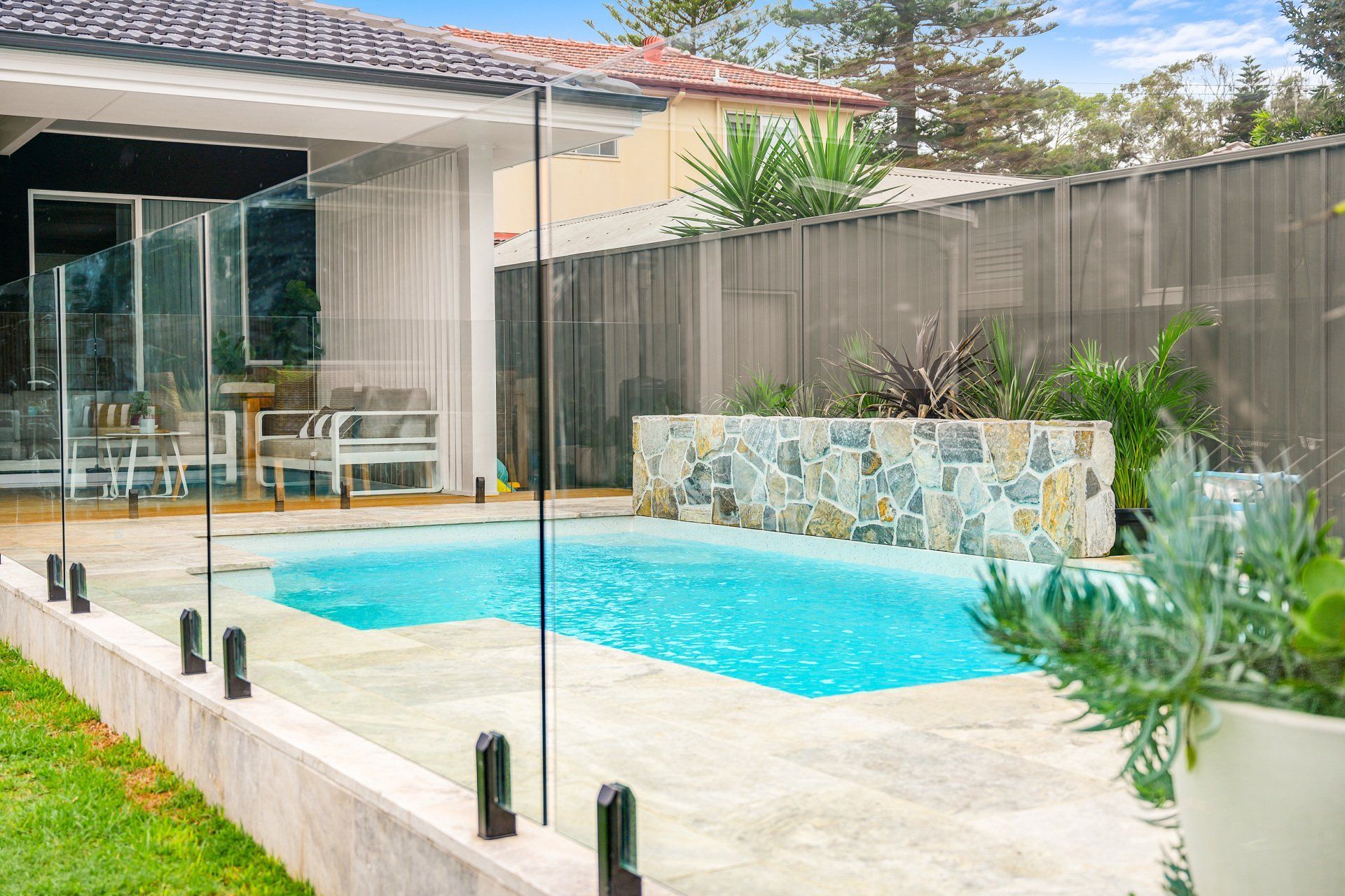 A swimming pool in the backyard of a house with a glass fence.