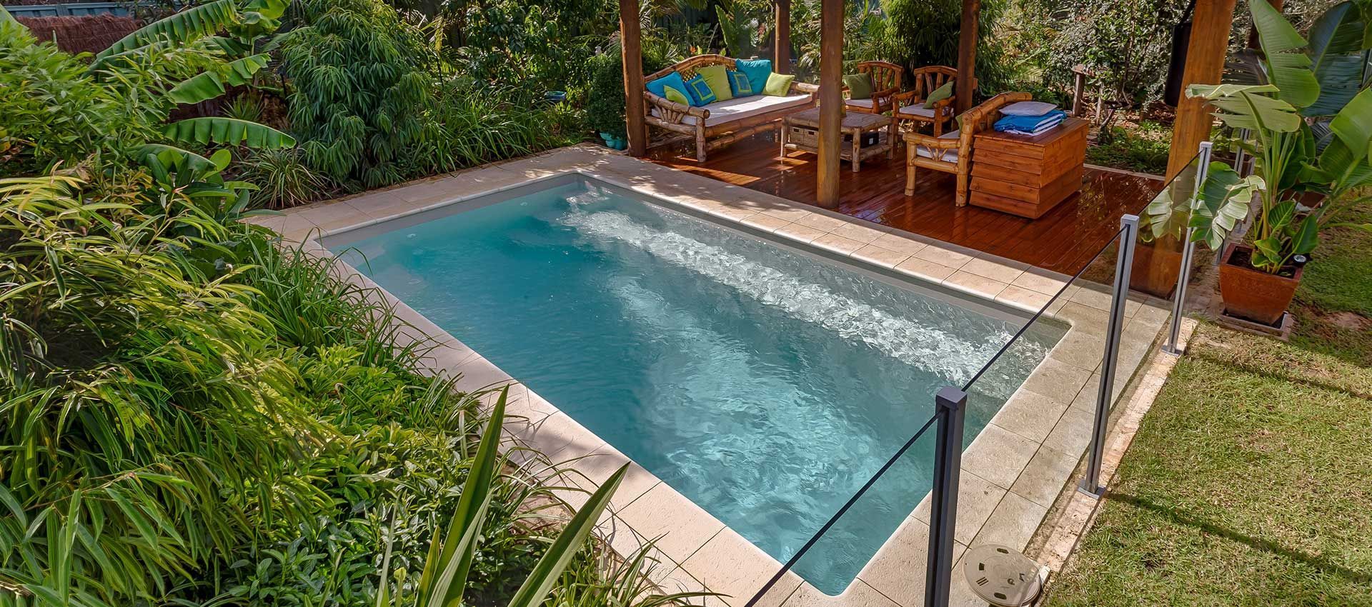 A small swimming pool is surrounded by lush greenery and a gazebo.