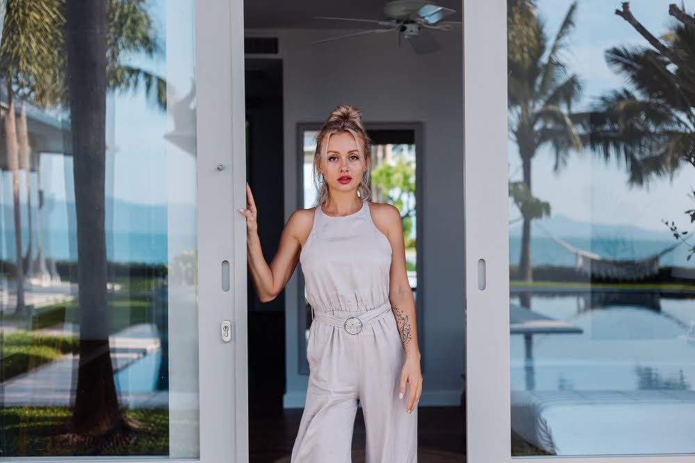 A woman standing by the doorway of a modern Miami home with tinted windows.