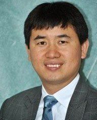 Smiling man in a gray suit and blue tie against a teal backdrop