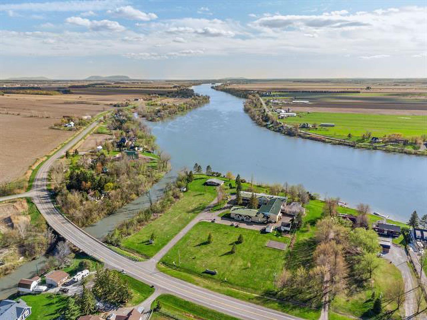 Vue aérienne d'une rivière serpentant à travers des terres agricoles bordées de routes, de champs verdoyants et de quelques maisons.