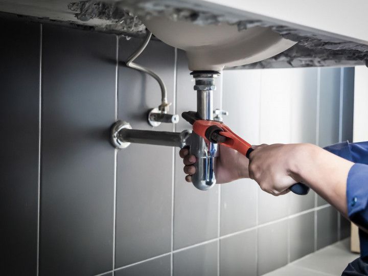 Plumber tightening a sink drain pipe under a bathroom sink with red pliers