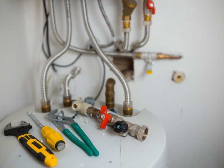 Plumbing tools and fittings on a sink or pipe workspace, with wrenches, pliers, and valves visible.
