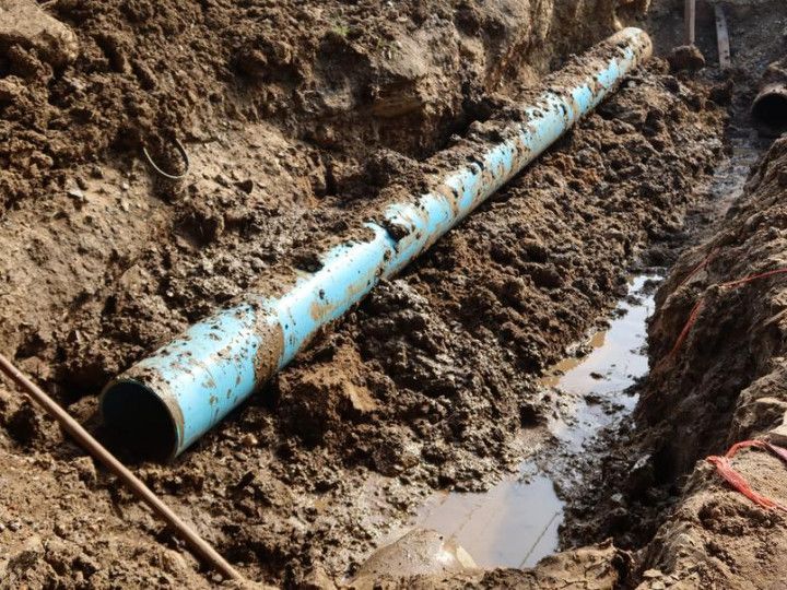Blue pipe exposed in a muddy trench with standing water.