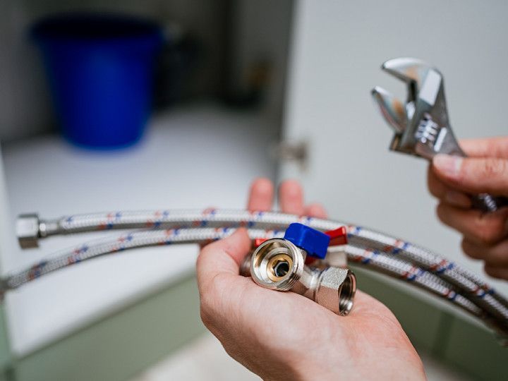 Hands holding a braided water hose with a metal fitting and wrench in a workshop setting