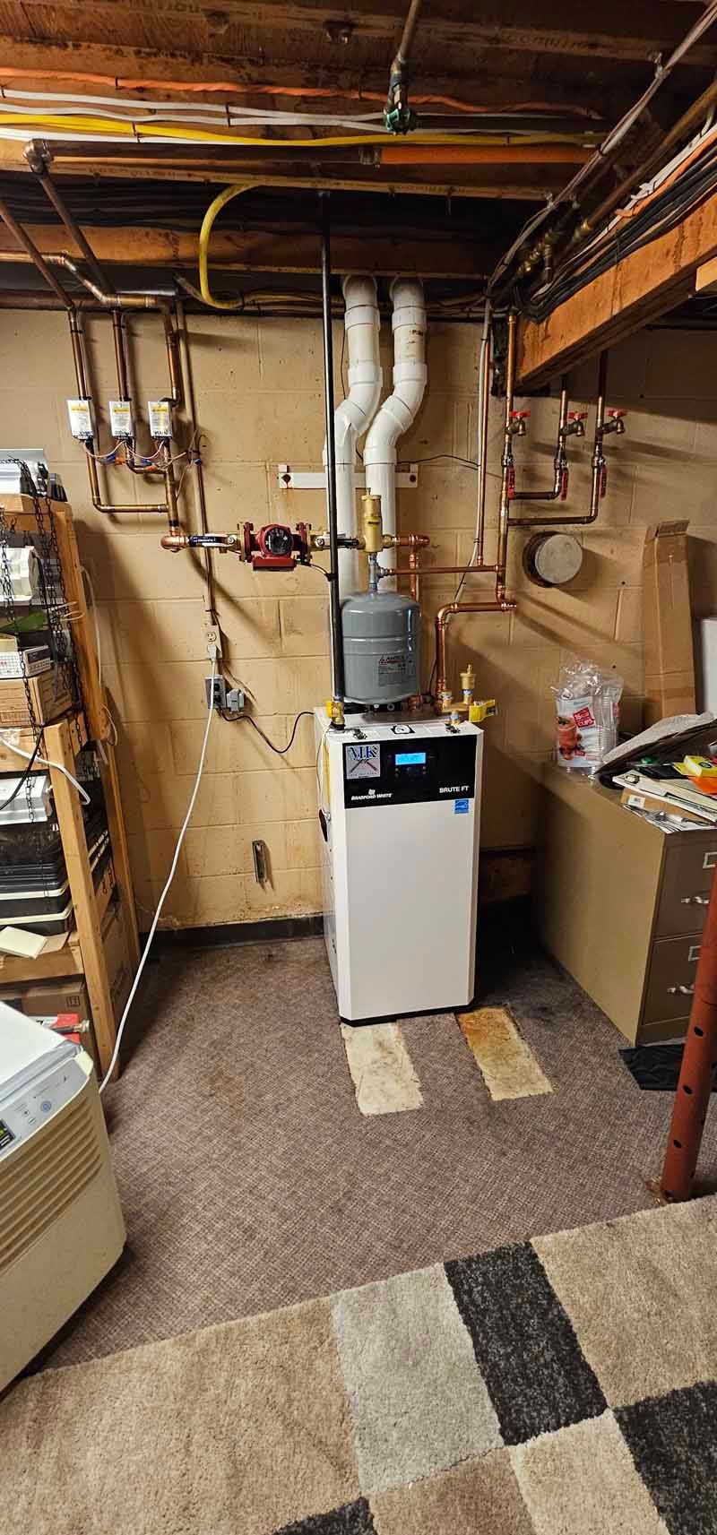 Basement utility room with a furnace, white vent pipes, exposed beams, and checkered carpet.