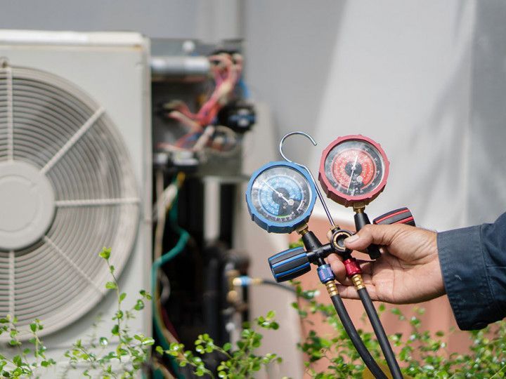 Hand holding HVAC manifold gauges beside an outdoor air conditioner unit