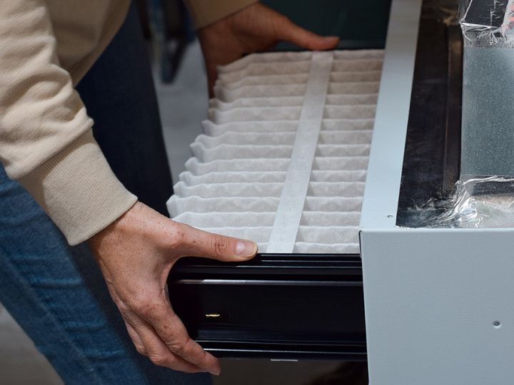 Hands loading white trays into a black machine drawer beside a gray metal unit