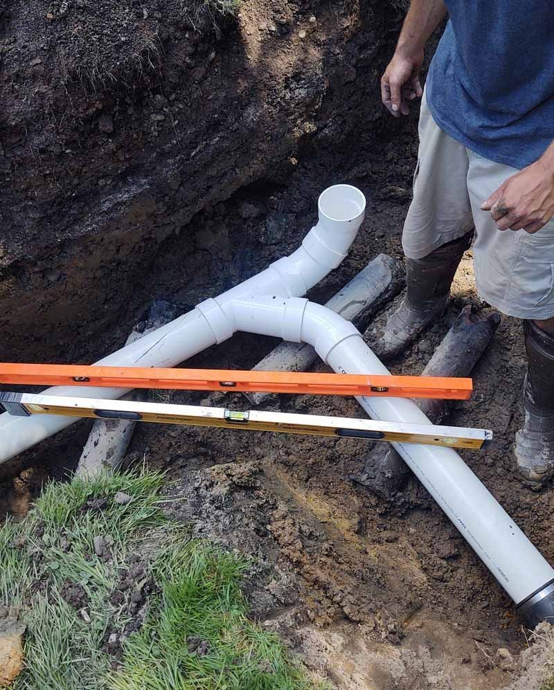 White PVC pipes installed in a muddy trench, with a person standing beside them.