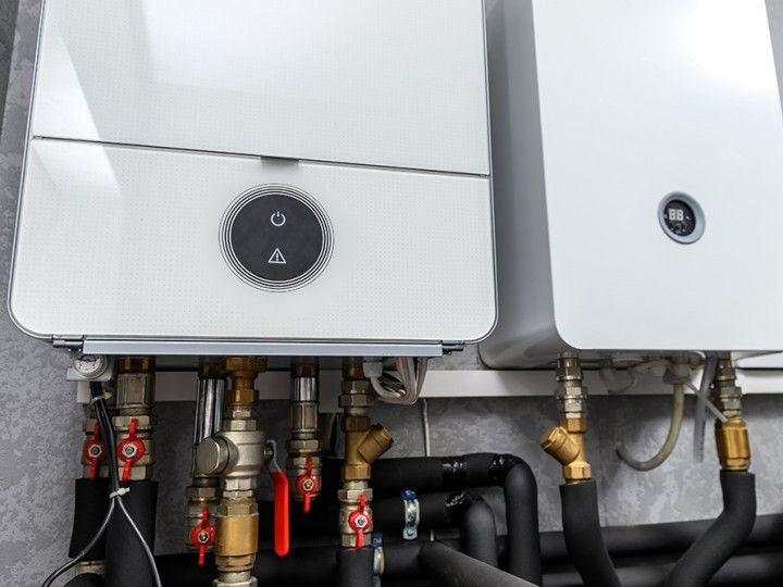 Two white wall-mounted boilers with pipes and valves underneath in a utility room
