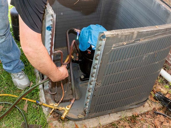 Technician servicing an outdoor air conditioner unit with tools and blue cloth nearby