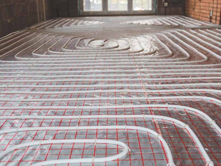 Coiled white pipes laid in a grid on a floor, forming a radiant heating system installation