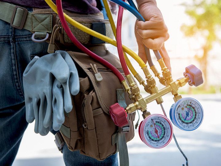 Close-up of a worker’s tool belt with gloves and HVAC manifold gauges connected to colored hoses