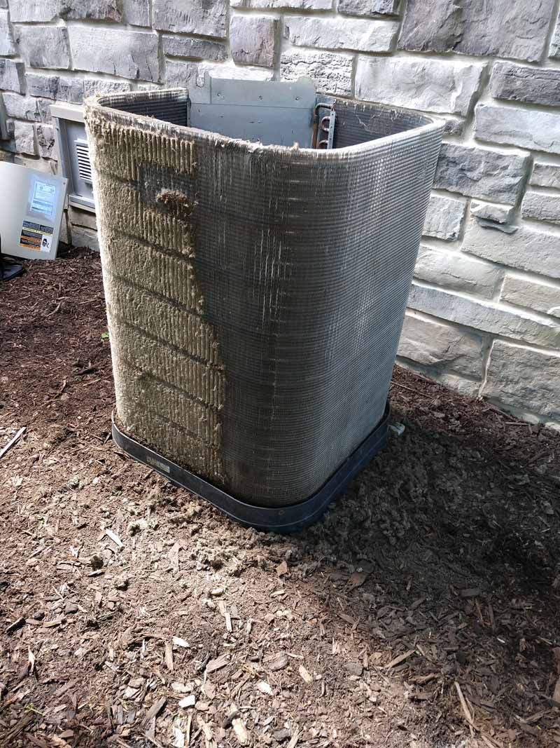 Outdoor HVAC unit with a protective cover beside a stone wall.
