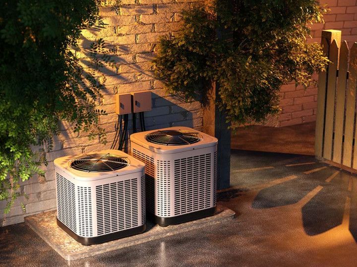 Two outdoor air conditioning units beside a brick wall, lit by warm evening light.