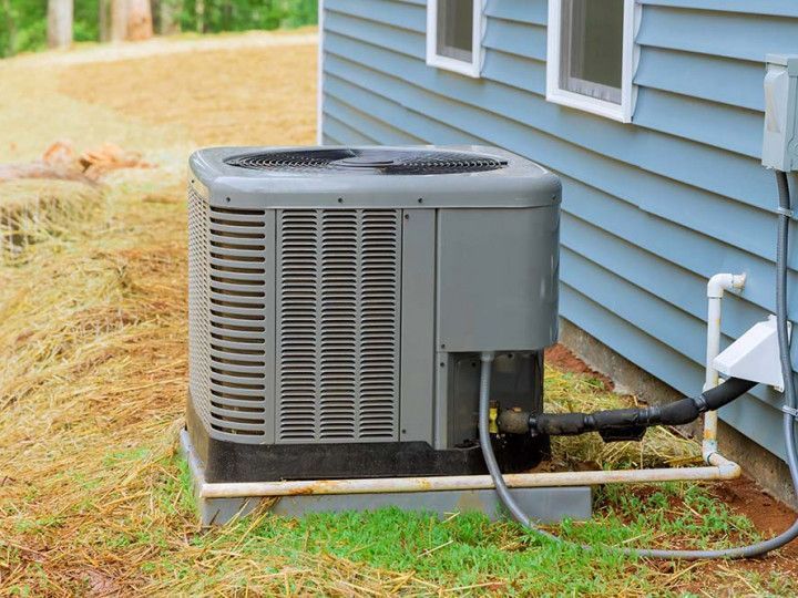Outdoor air conditioner unit beside a blue house with connected pipes and hose