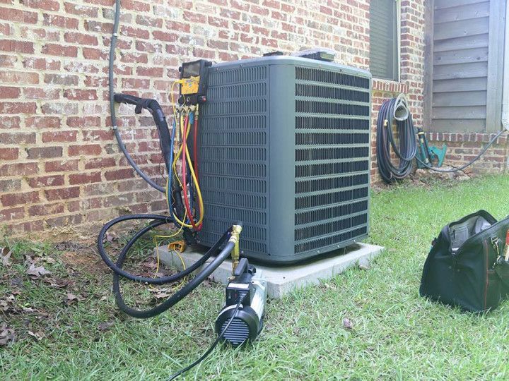 Outdoor air conditioner unit with hoses and a small pump beside a brick house wall
