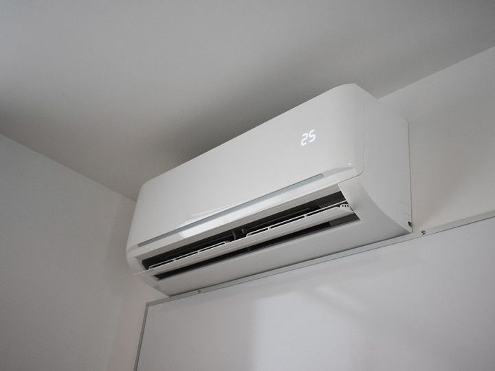 White wall-mounted air conditioner on a pale wall, showing a digital temperature display.