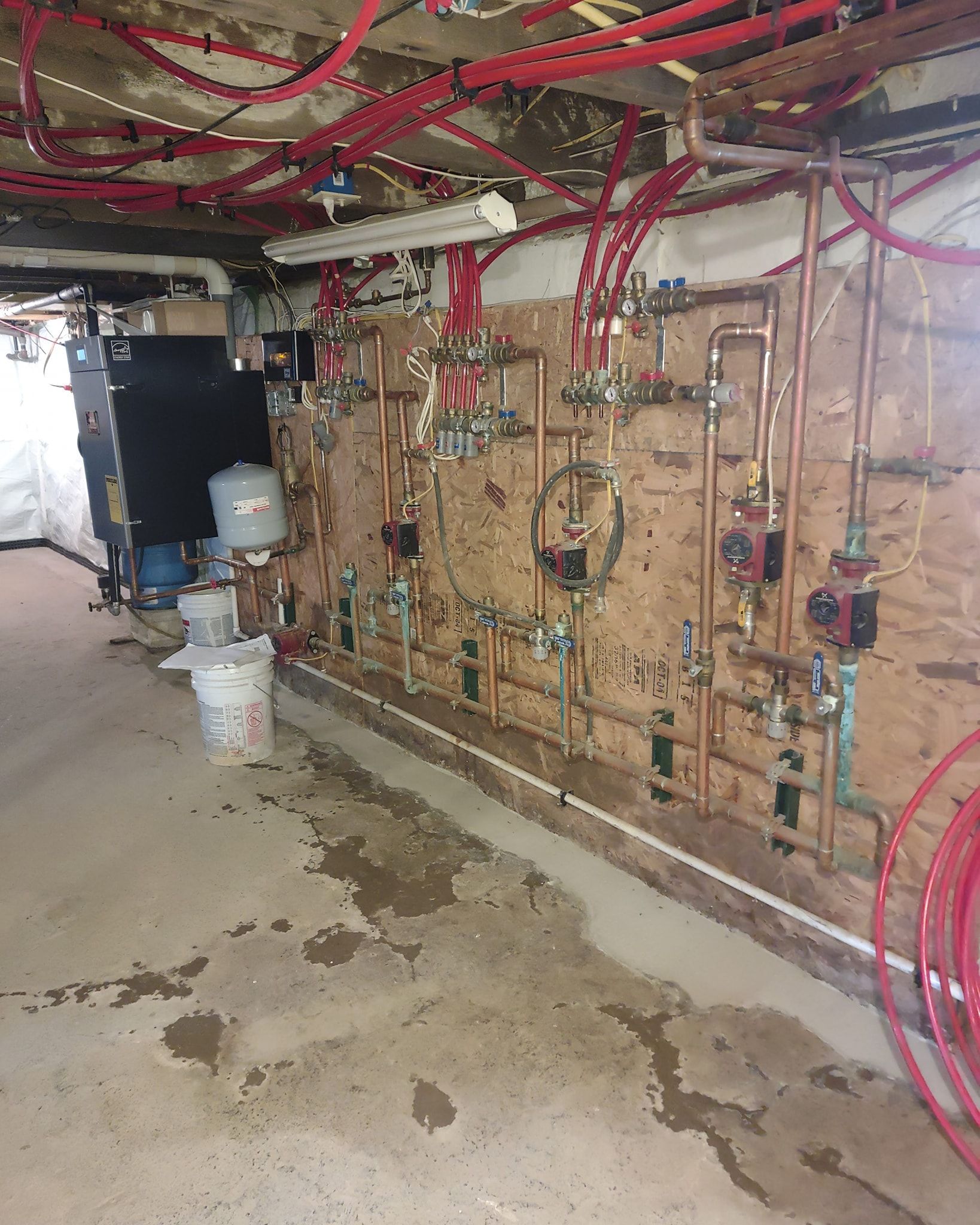Basement utility room with exposed red pipes, valves, and wet concrete floor.