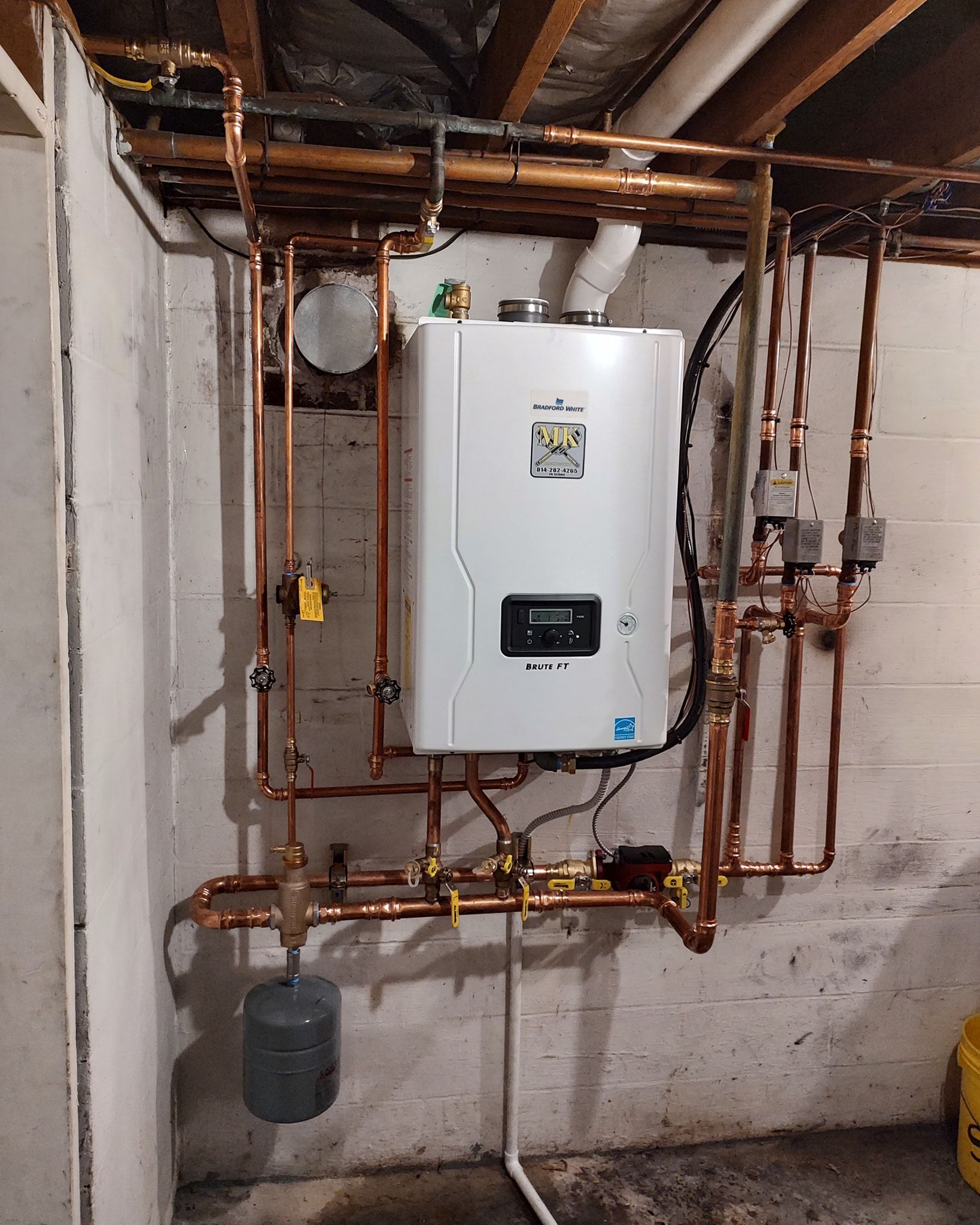 Wall-mounted white boiler with copper pipes in a basement utility room.
