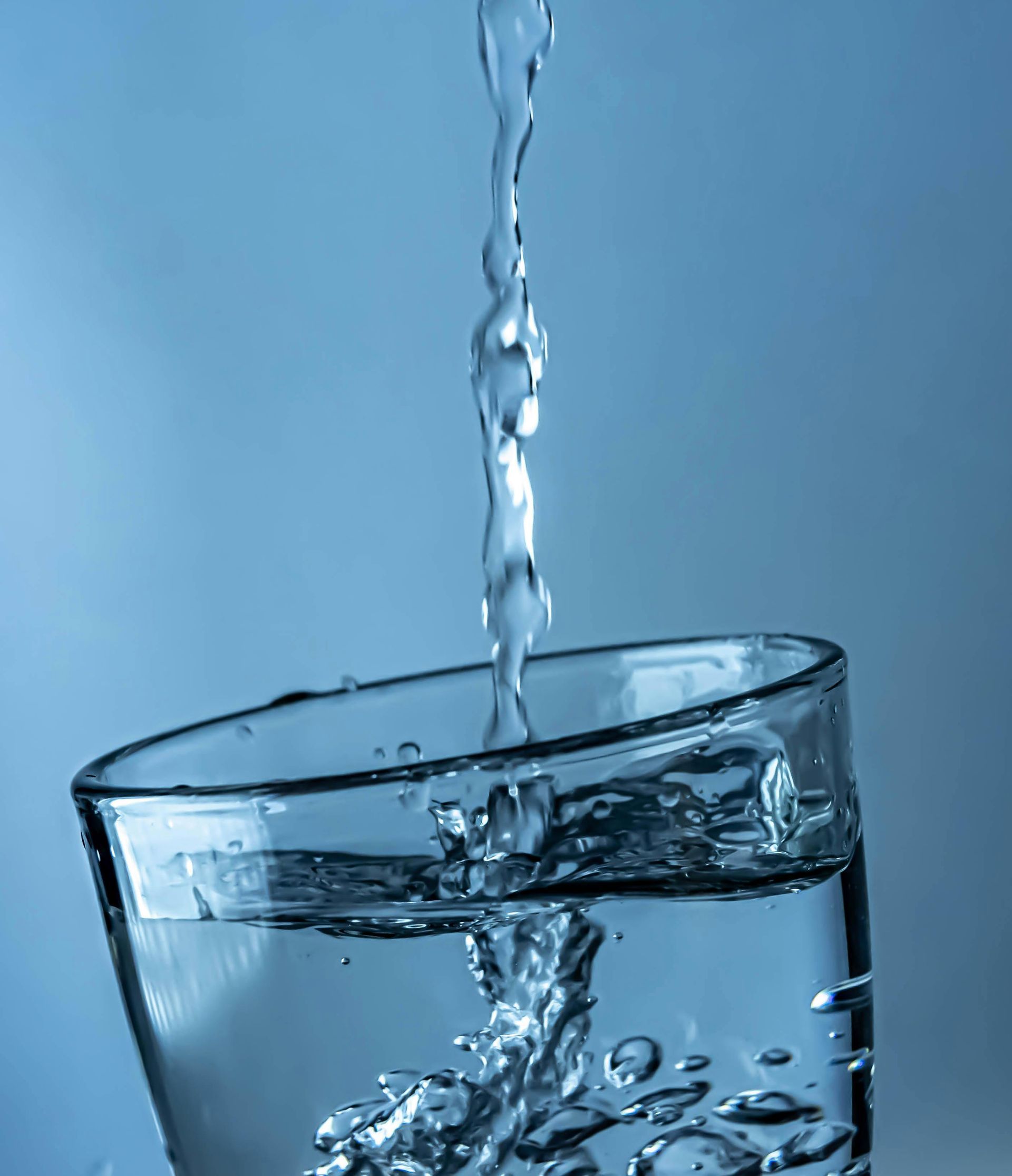 Water pouring into a clear glass against a blue background