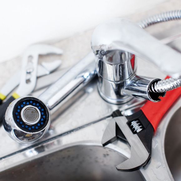 Chrome faucet, adjustable wrench, and screwdriver on a sink during plumbing repair