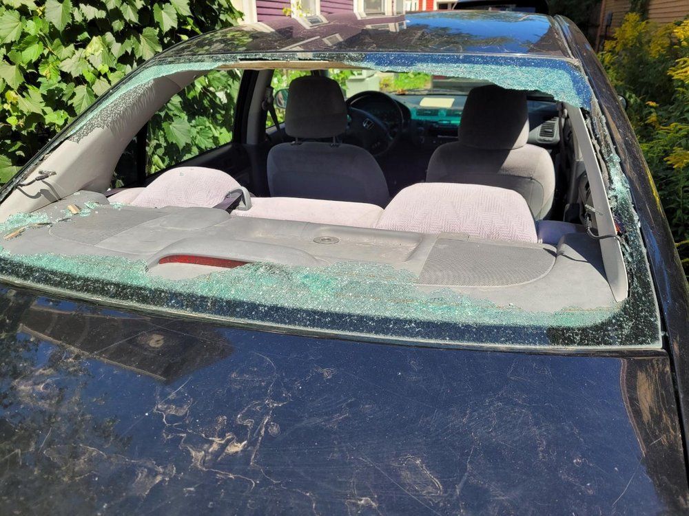 A black car with a broken windshield is parked in front of a house
