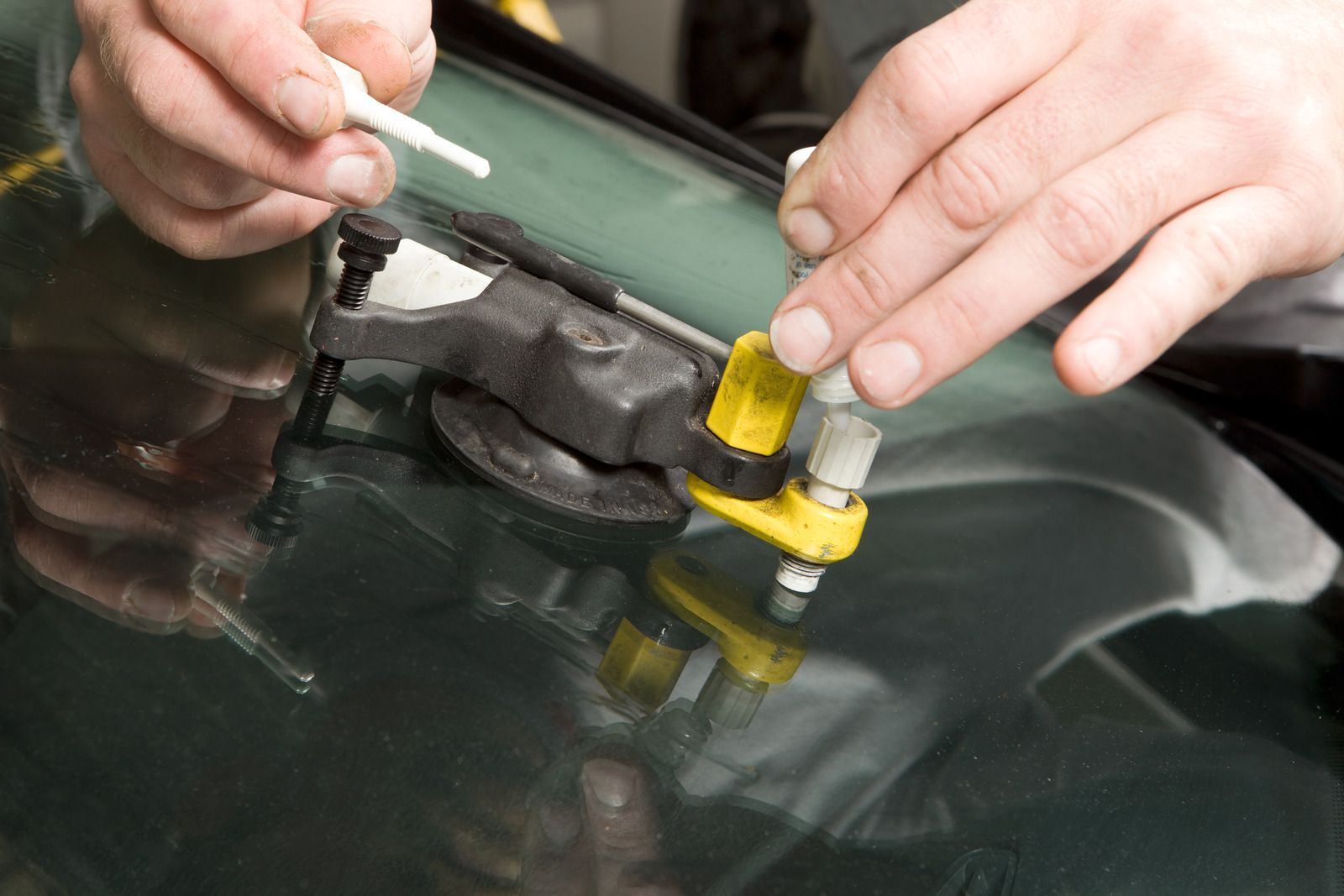 A person is repairing a windshield on a car with a tool.