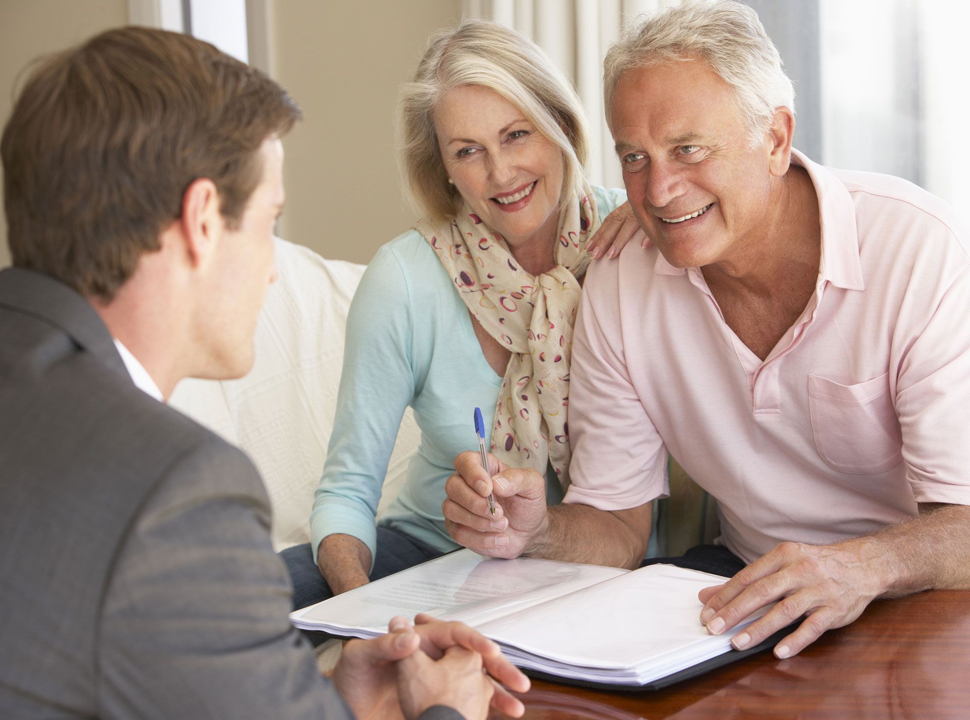 An older man and women smile as they complete forms with a lawyer
