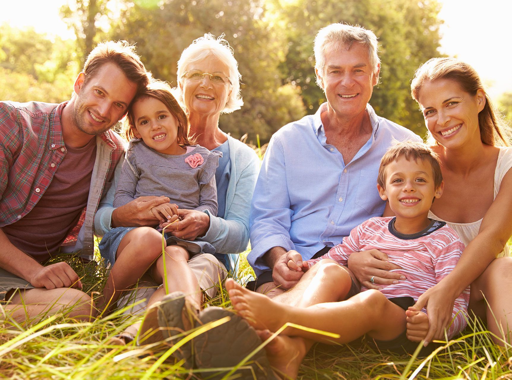 A happy family sitting outside, including parents, young children, and two grandparents