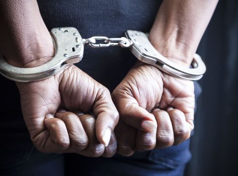 Man in handcuffs with hands clasped, sitting at a table, likely in an interrogation room.