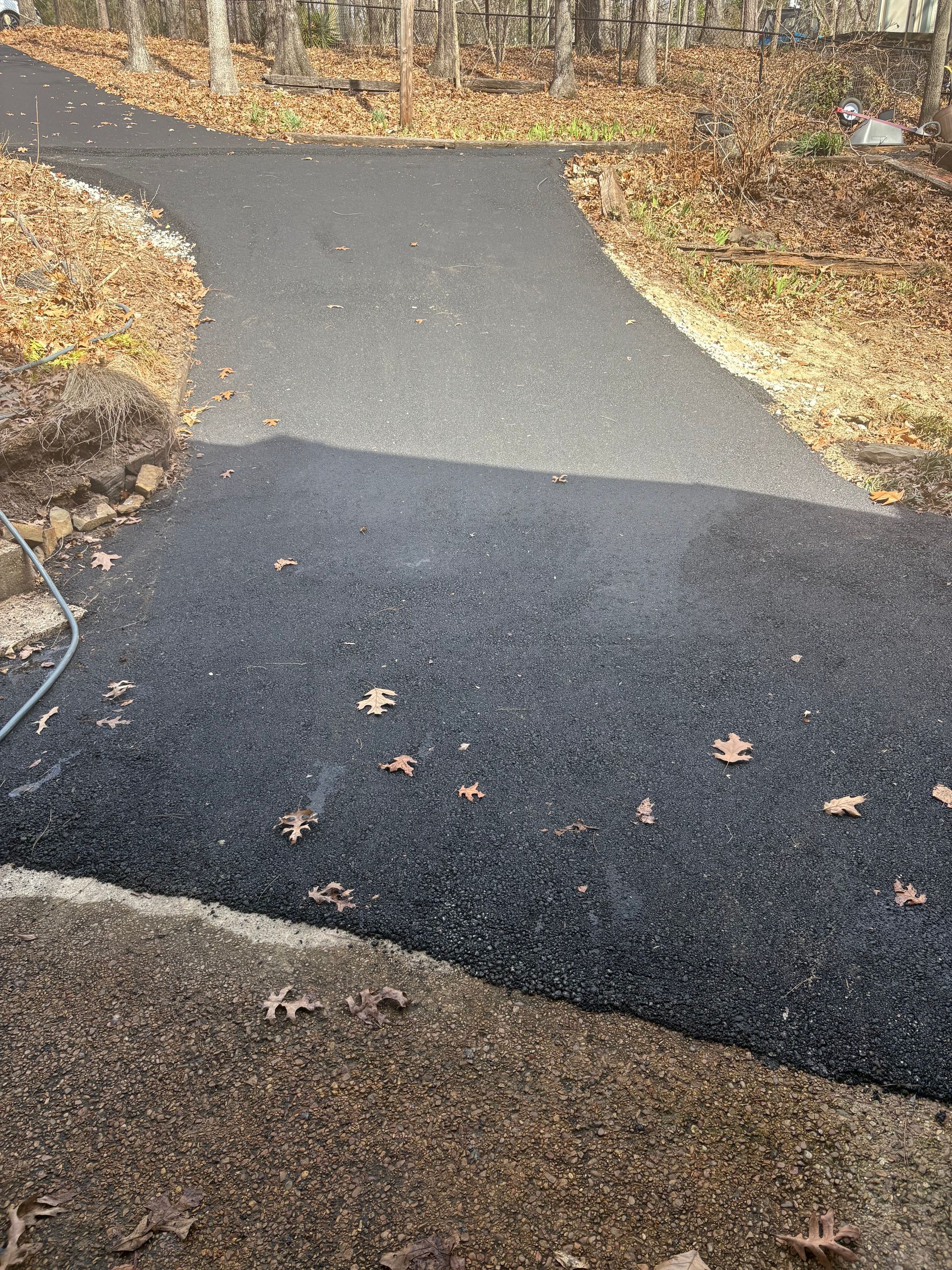 Freshly paved black asphalt driveway splitting into two directions, with fallen leaves.