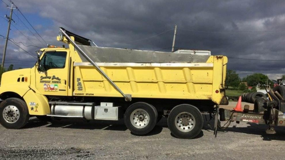 Yellow dump truck parked on asphalt under a cloudy sky.