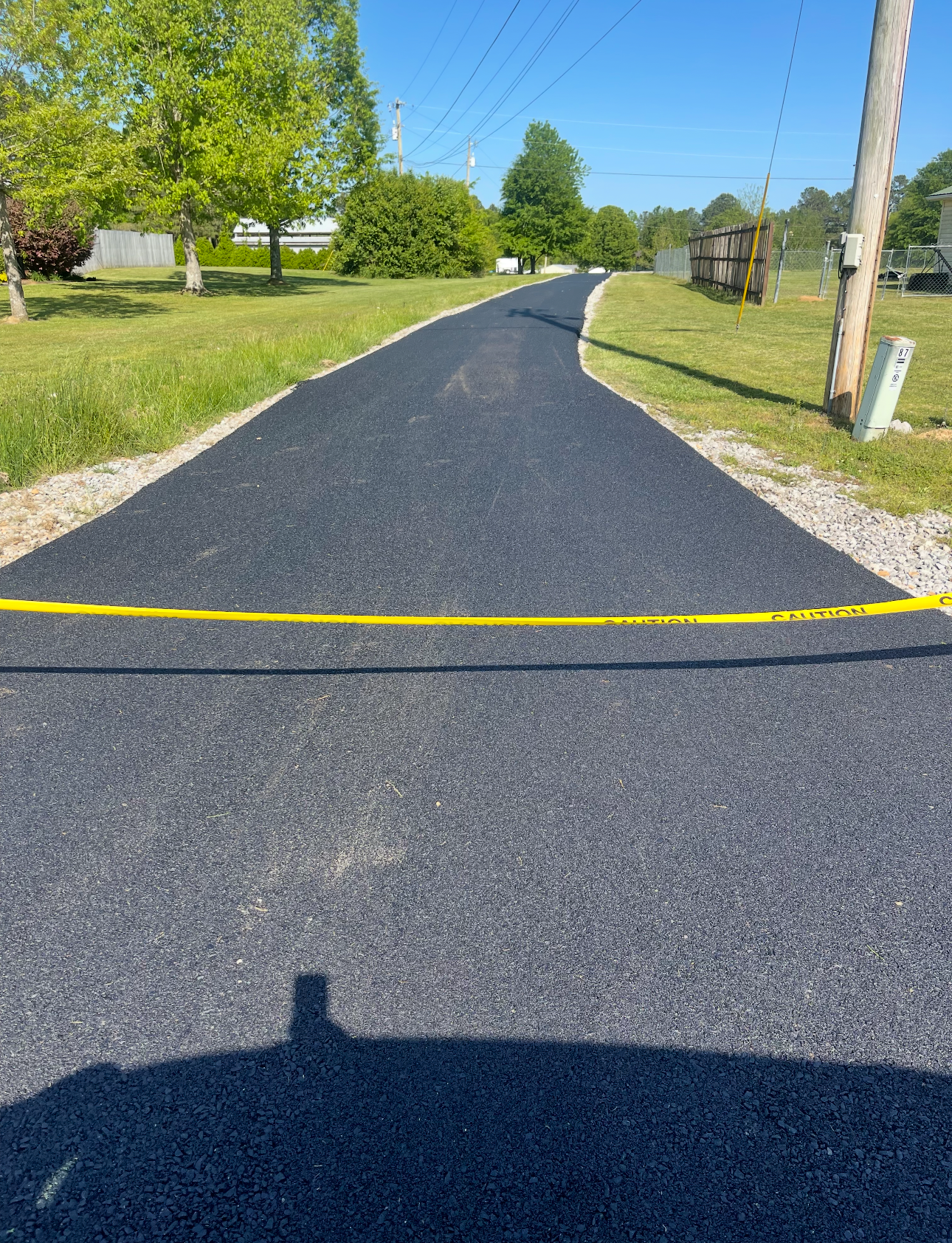 Road worker smoothing fresh asphalt with shovel next to a steamroller.