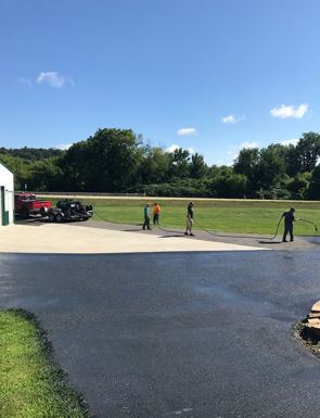 Workers sealcoating asphalt driveway on a sunny day.