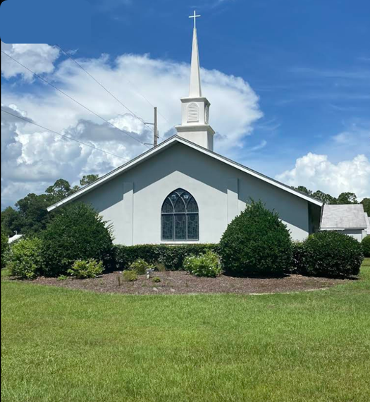 White church building with a steeple and cross against a blue sky.