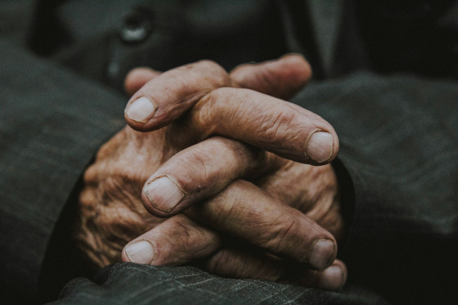 Ineengevouwen handen rustend op een donker oppervlak; vingers in elkaar verstrengeld.