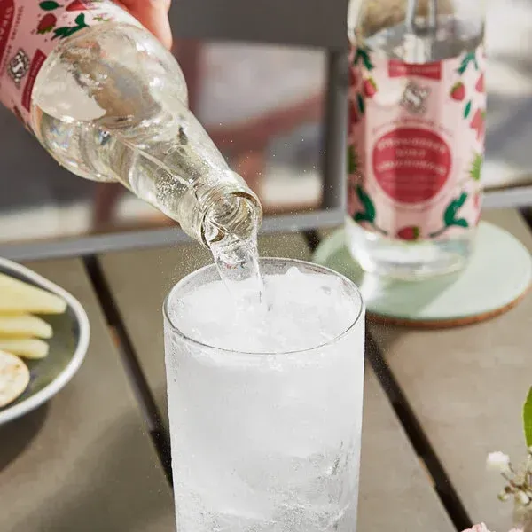 Clear drink being poured into a frosty glass on a table, with another bottle in the background.