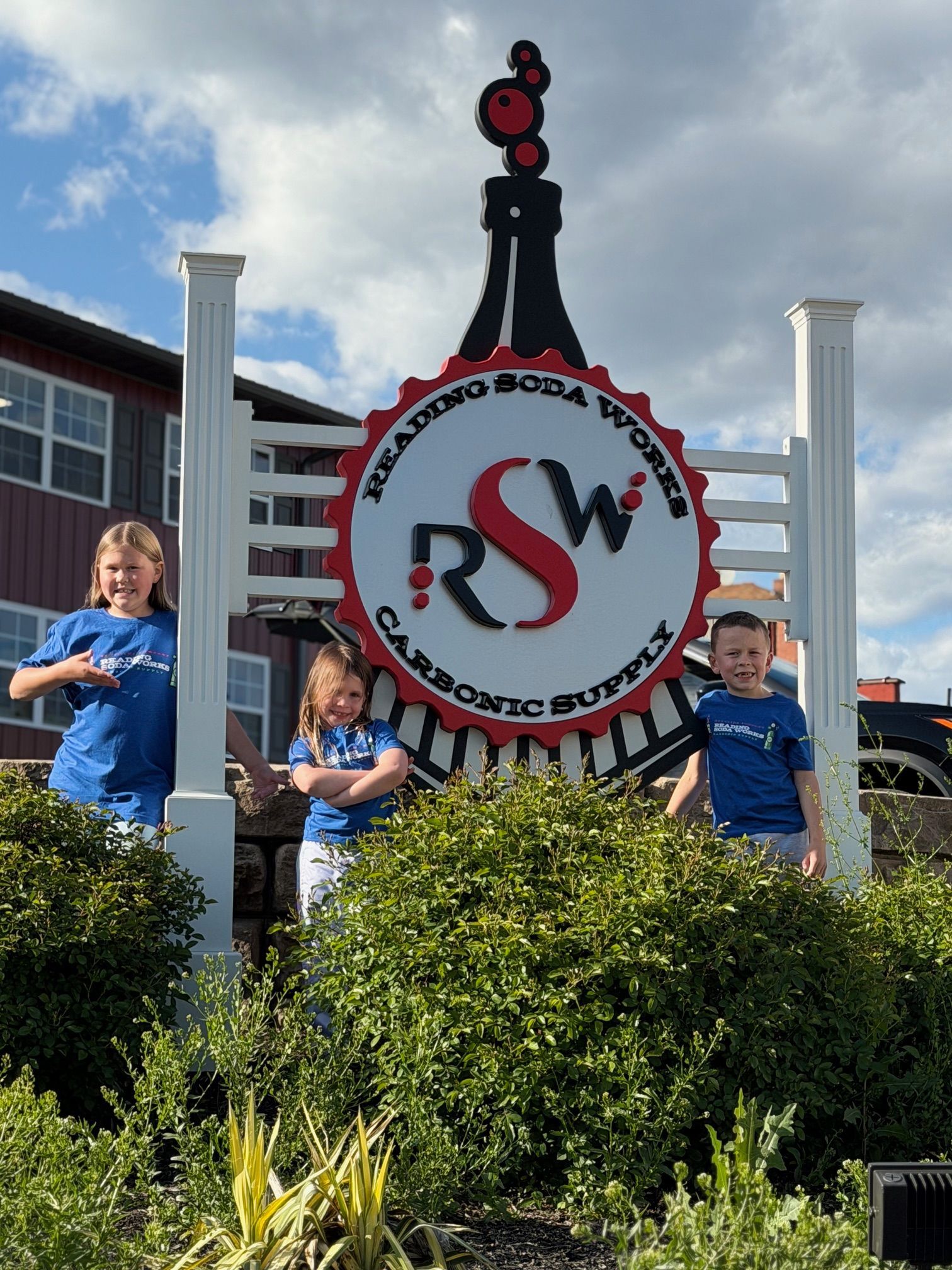 Three children posing by a large RSW train sign in a garden area