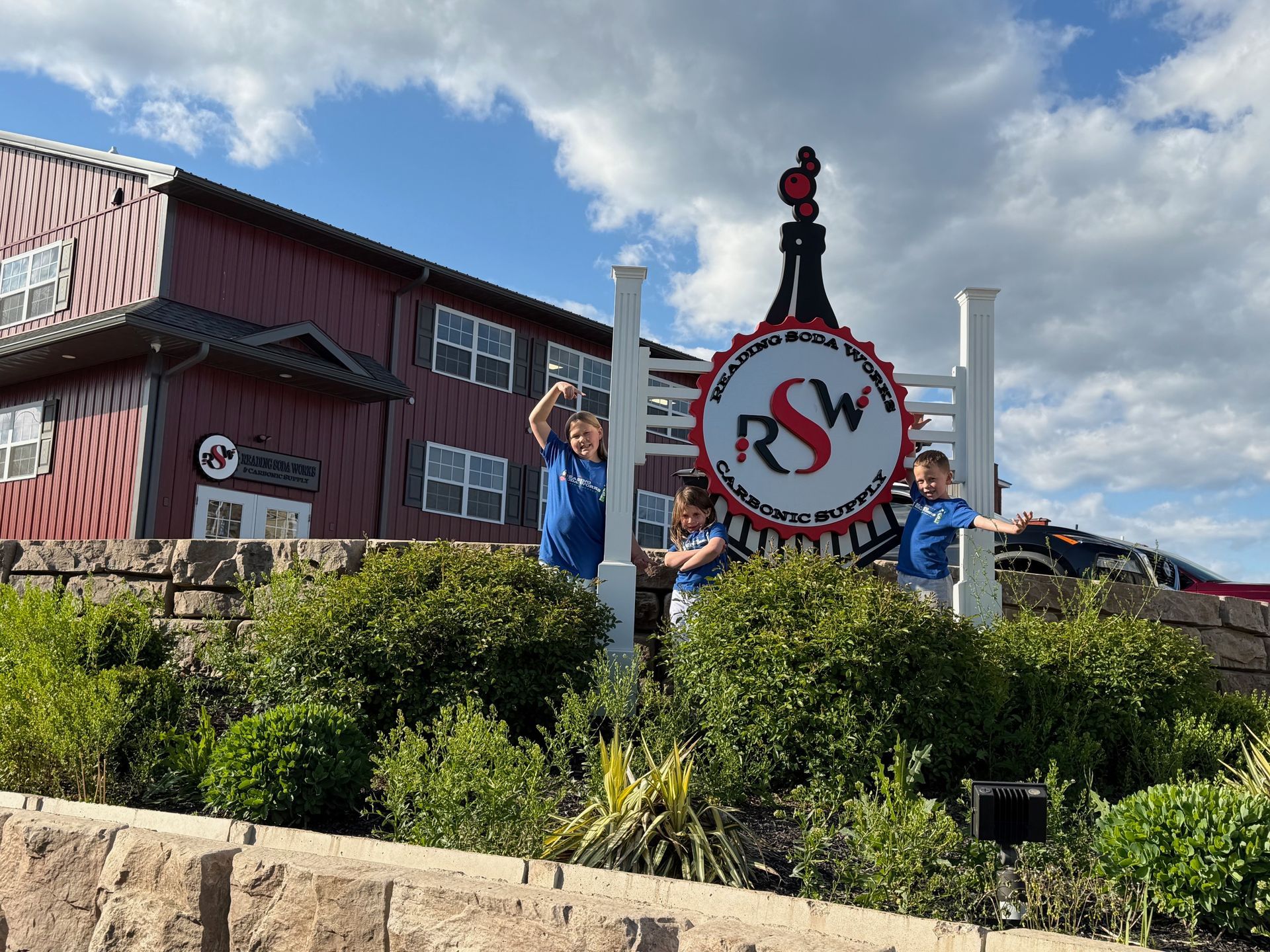 People posing by a large E.R.W. gear sign in front of a red building under a blue sky.