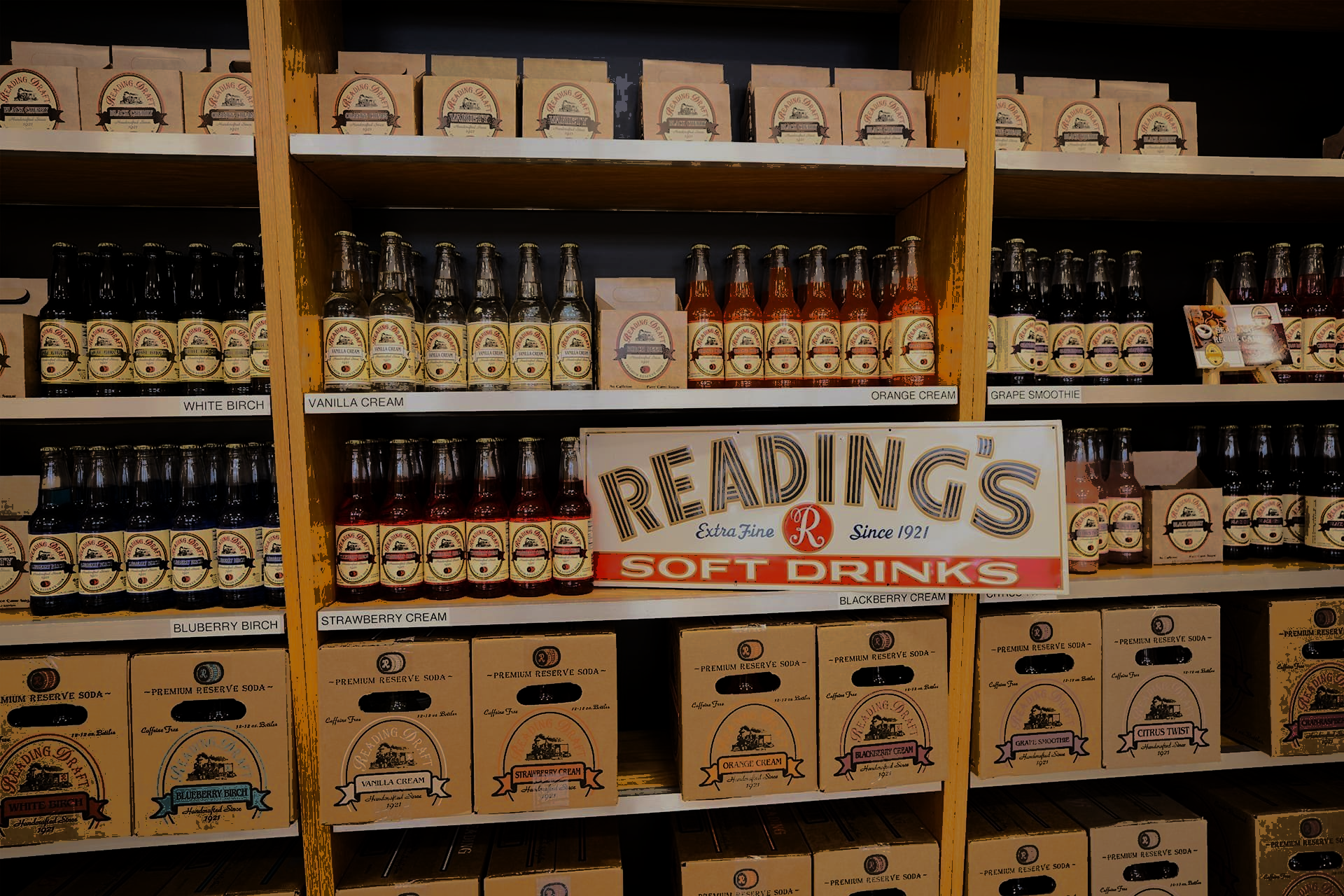 Shelves stocked with bottled drinks and wooden crates, with a “Reading” sign in the center.