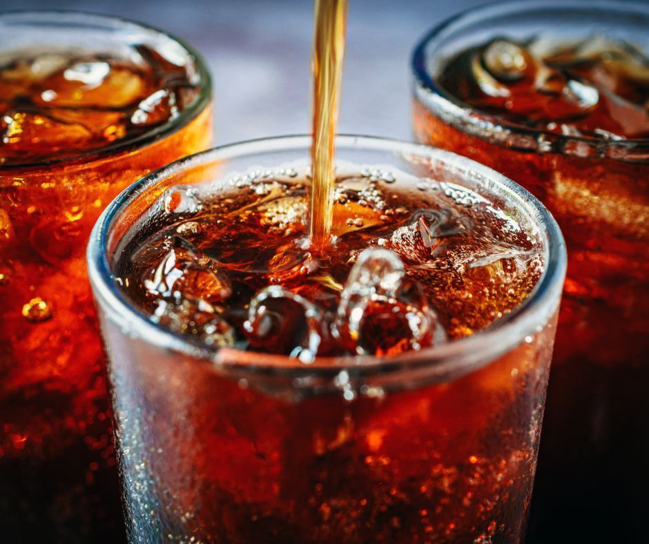 Three glasses of dark soda with ice, one being poured from above