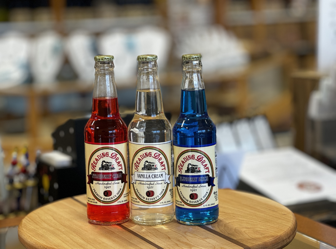 Three small bottled drinks—red, clear, and blue—arranged on a wooden table in a shop.