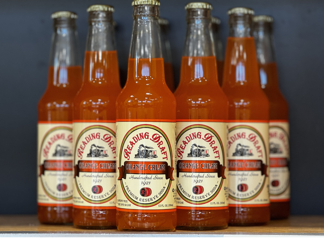 Six orange soda bottles with cream labels lined up on a shelf