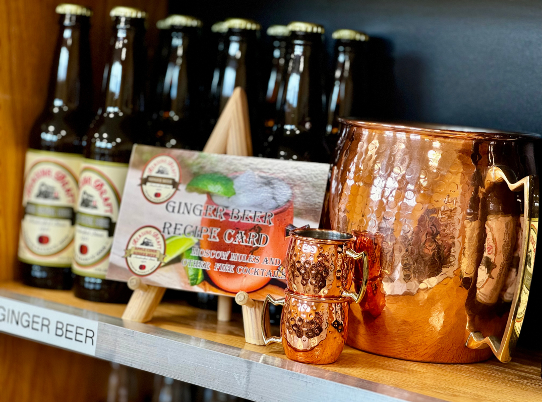 Ginger beer bottles and copper mugs on a shelf, with a ginger beer sign