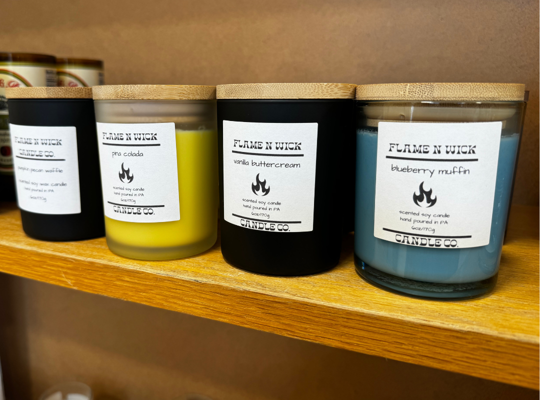 Four labeled candles in clear, yellow, black, and gray jars on a wooden shelf.
