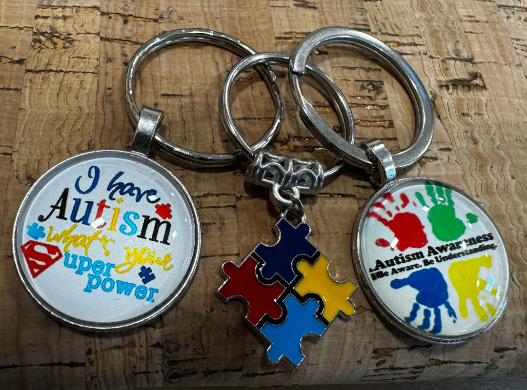 Autism awareness keychains with colorful puzzle pieces and handprint designs on a wooden surface