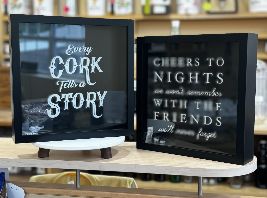 Two black framed signs on white stands with wedding quotes, one reading “Every cork has a story.”